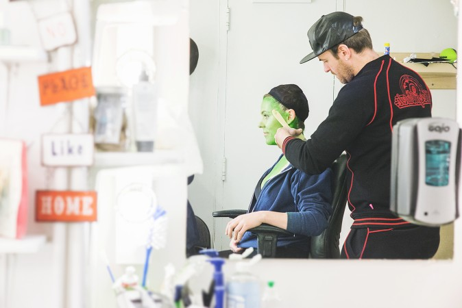 A theatre make-up artist applying green makeup to transform an actress into Elphaba in Wicked