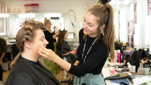 Make-up artist works applying foundation to a model with period hair style in a studio